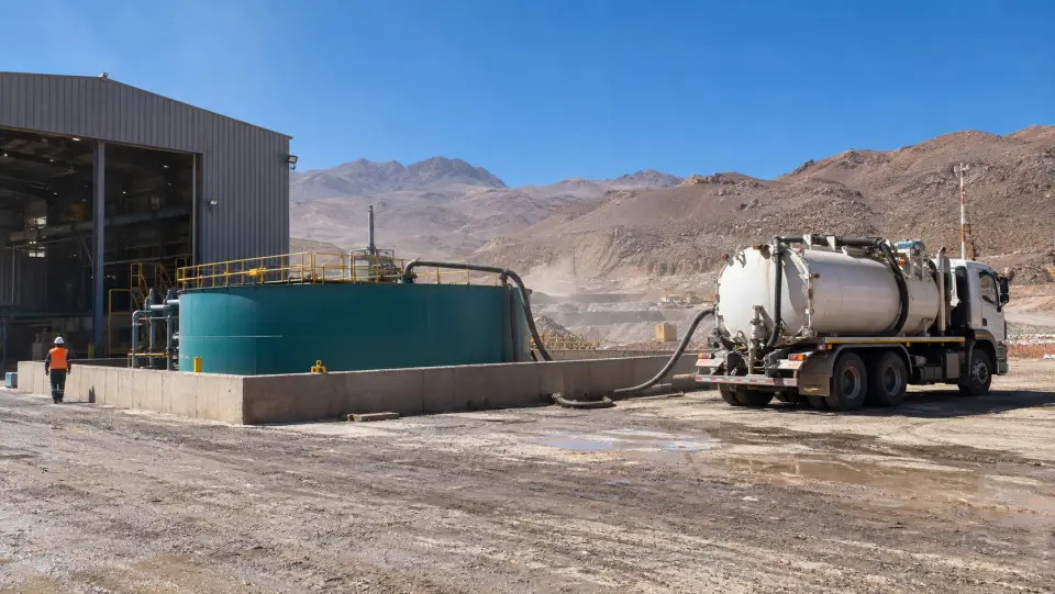 Camión succionador conectado a un estanque de acopio con pretil junto a un galpón de una faena en el desierto