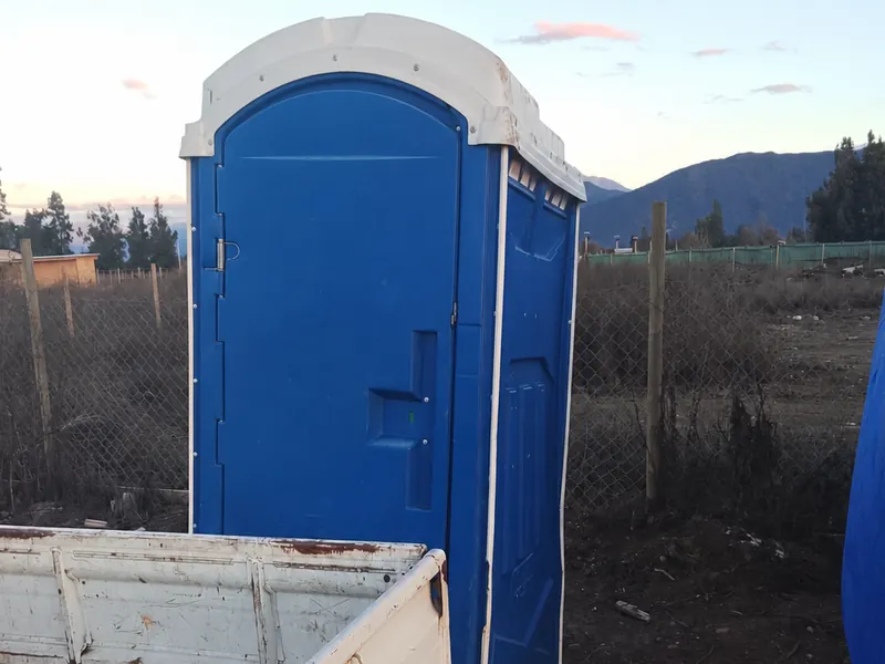 Baño químico azul junto a la camioneta de reparto, listo para cargar